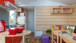 Une cuisine compacte équipée d’une cuisinière, d’un four à micro-ondes et d’un petit réfrigérateur. On y trouve également un coin repas avec une table et des chaises, ainsi qu’un banc agrémenté d’un coussin à motifs floraux.