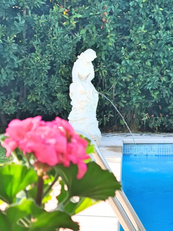 A statue by a poolside with a hedge in the background.