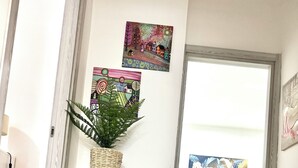 Ein Zimmer mit Holzboden, einem weißen Schrank mit Schubladen, einer Topfpflanze und einem Bett mit grüner Decke.