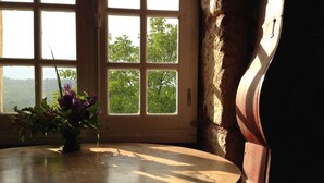 A room with a round wooden table, a potted plant with purple flowers, and a view of trees through a window. - House with character with swimming-pool  (Belvès)
