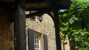 A rustic stone building with a wooden door and black shutters, a stone wall, and a vine-covered trellis. - House with character with swimming-pool  (Belvès)
