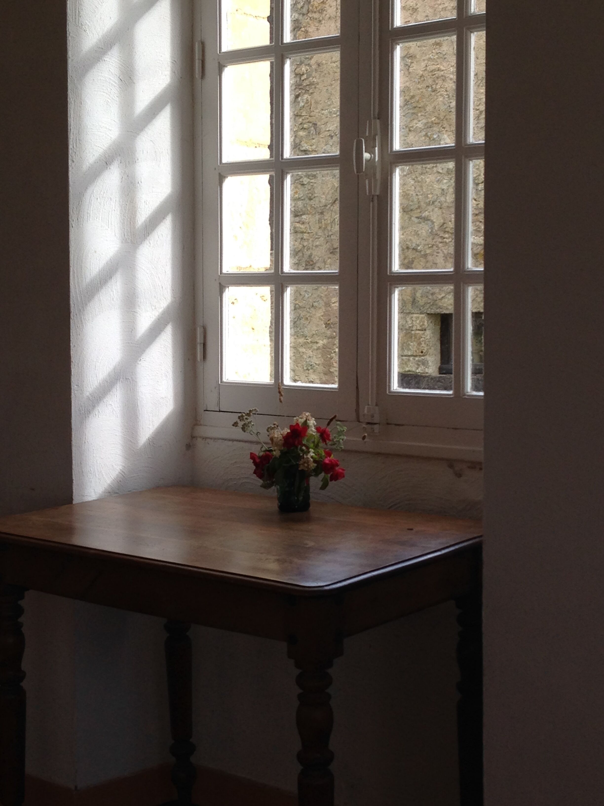 A corner with a wooden table and a vase of flowers by a window with white frames.