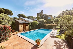 A swimming pool with a tiled deck, a small shed, and a lawn chair.