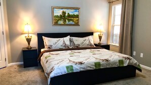 A bedroom with a bed, two bedside lamps, a framed painting, and a window with curtains. - Jacksonville Vacation (Jacksonville)
