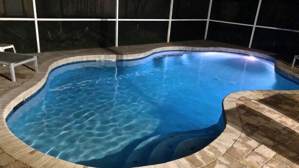 A swimming pool with a curved edge and a tiled deck surrounding it. - Jacksonville Vacation (Jacksonville)
