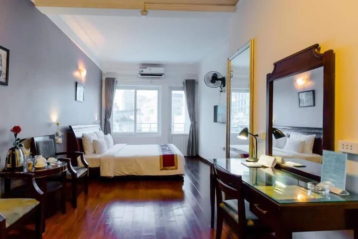 A hotel room with a bed, desk, chair, and a large mirror.