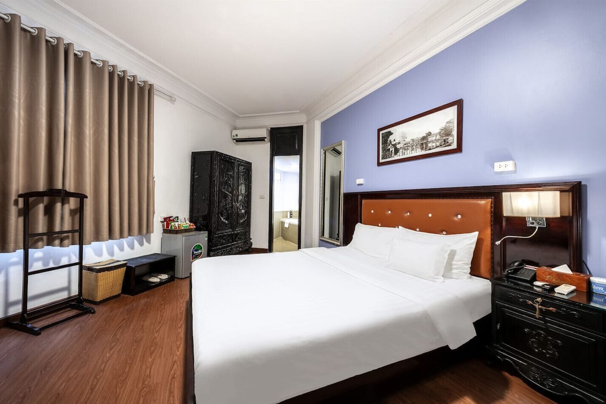 A hotel room with a large bed, a wardrobe, a desk with a lamp, and a picture on the wall.