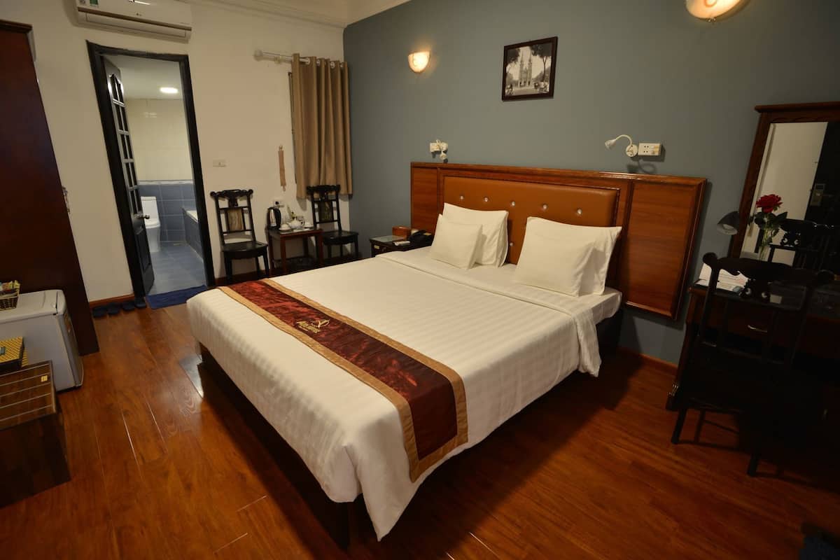 A hotel room with a large bed, wooden headboard, a nightstand, a desk, and a chair.