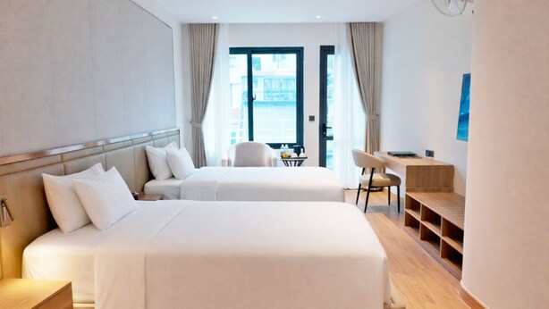 A hotel room with two beds, a desk, a chair, and a view of the city.