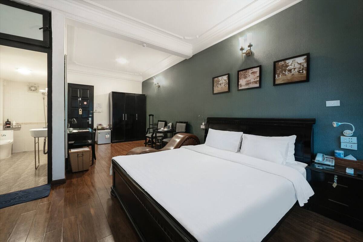 A hotel room with a large bed, a desk, a chair, a wardrobe, and a bathroom visible through an open door.