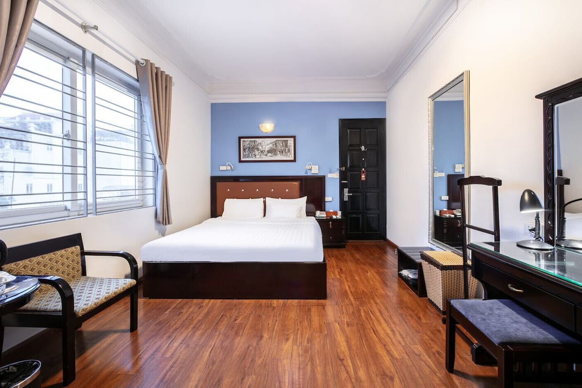 A hotel room with a large bed, a desk with a mirror, a chair, and a window with curtains.