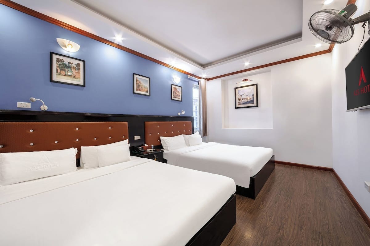 A hotel room with two beds, a ceiling fan, and artwork on the walls.