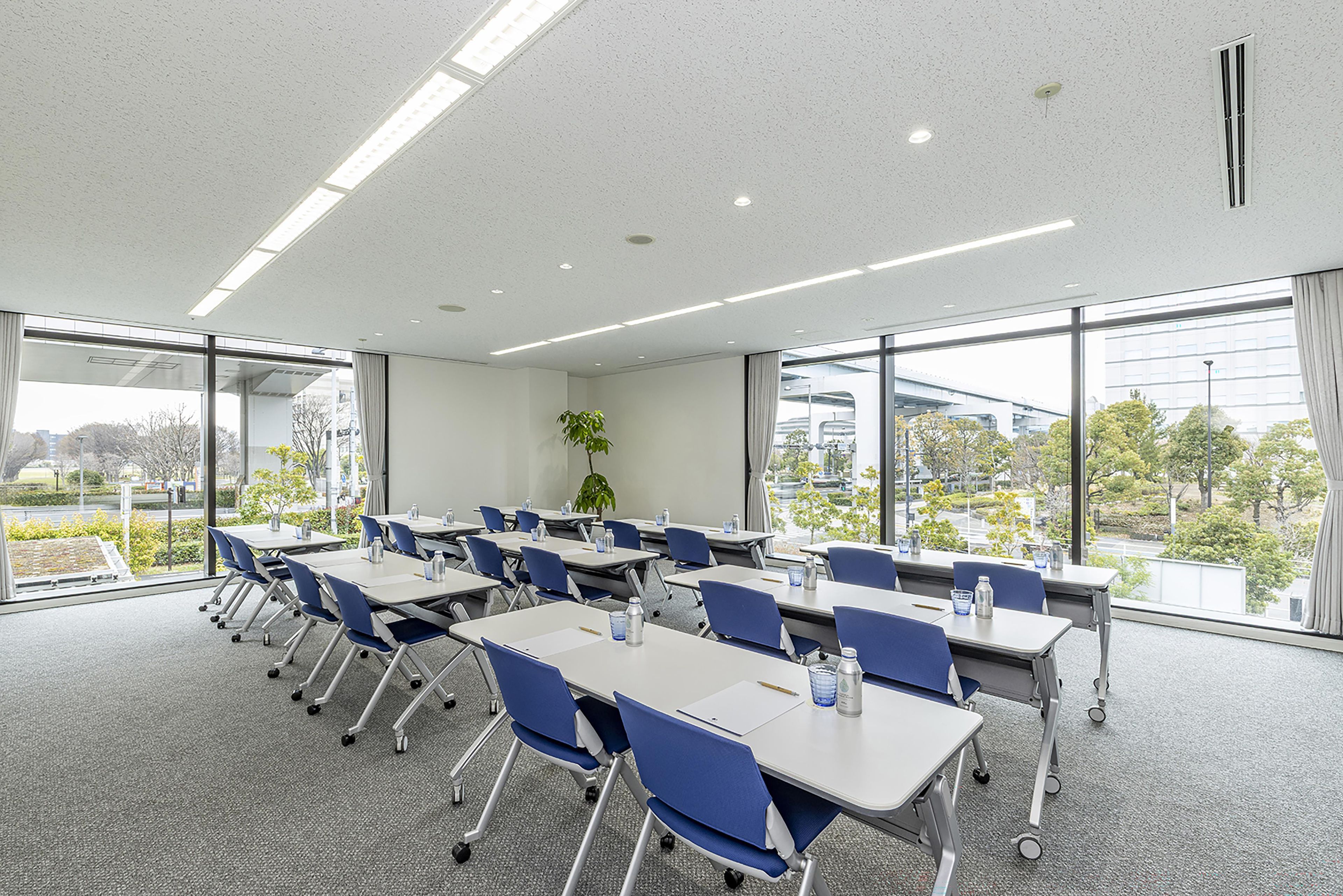 Een vergaderzaal met tafels, stoelen, grote ramen en een plant.
