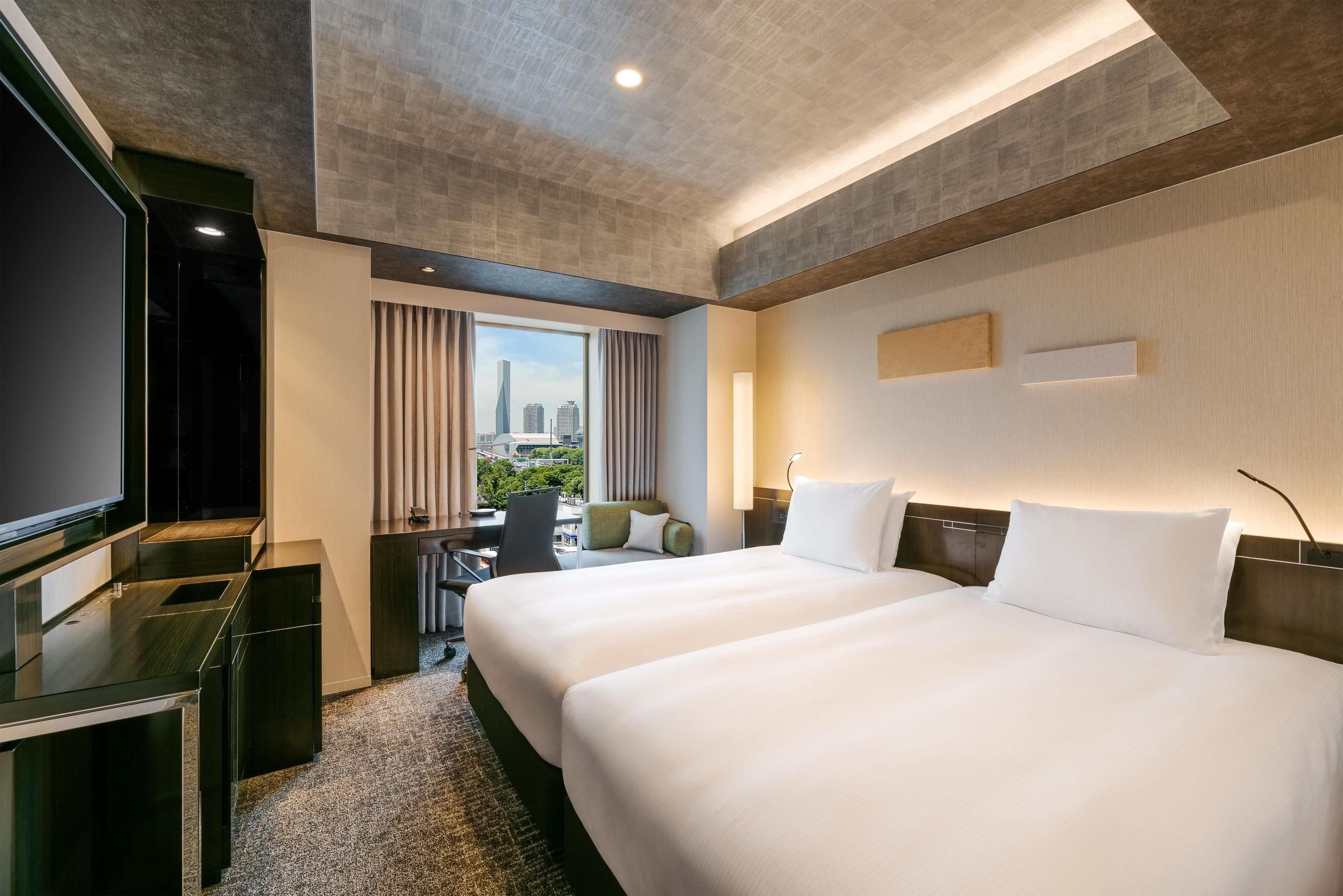 A hotel room with a large bed, a desk, a television, and a view of the city.