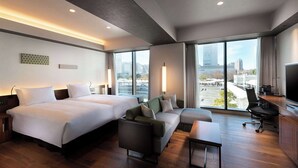 A hotel room with two beds, a sofa, a desk, and a TV. The room has large windows with a city view. - DoubleTree by Hilton Tokyo Ariake (Tokyo)