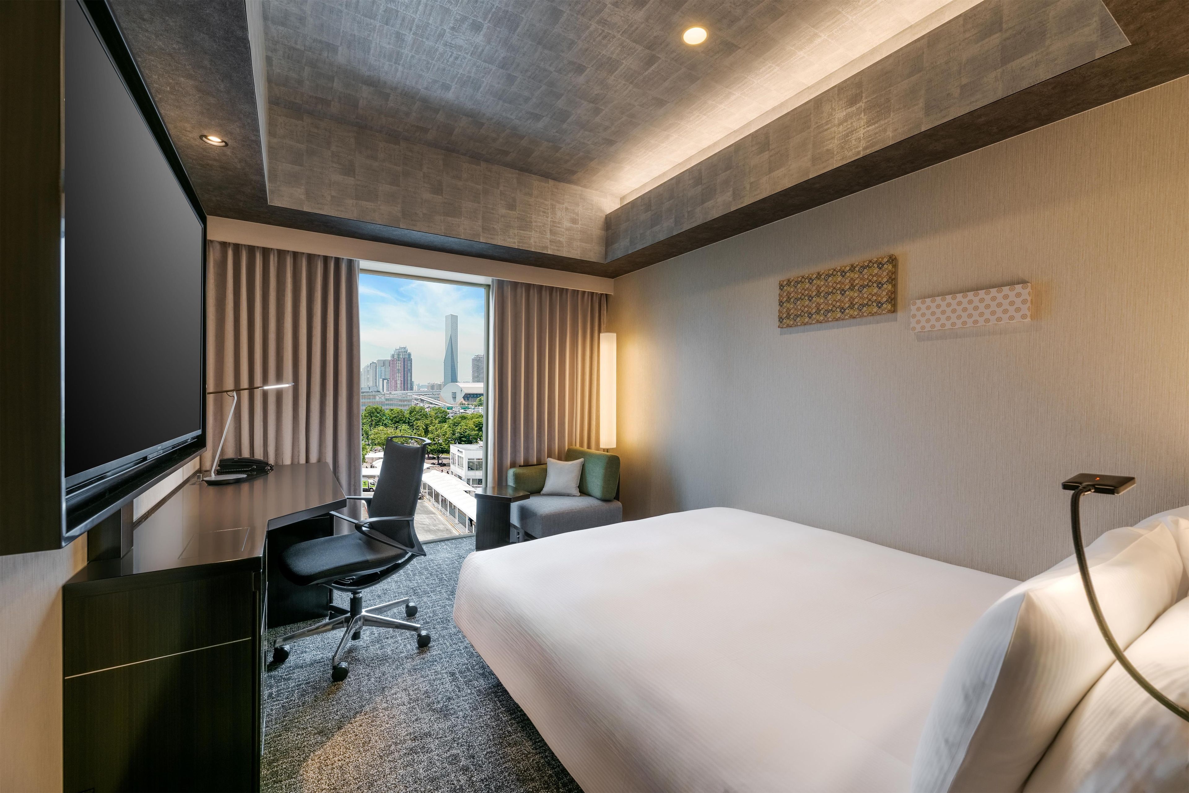 A hotel room with a bed, desk, chair, and a TV.