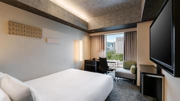 A hotel room with a bed, desk, chair, and a large TV screen.