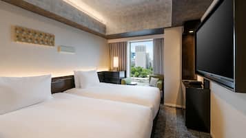 A hotel room with two beds, a TV, a desk, and a window with a city view.