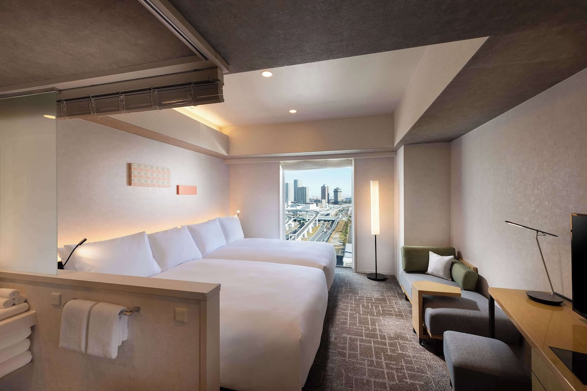 A hotel room with two beds, a sofa, a desk, and a TV.
