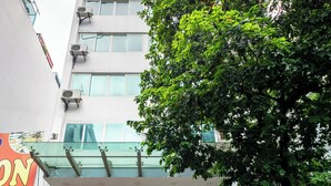A modern building with a glass entrance, a red carpet leading to the door, and a tree in front. - A25 Hotel - Dich Vong Hau (Hanoi)