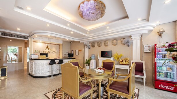 A hotel lobby with a reception desk, a dining area with a round table and chairs, a red Coca-Cola refrigerator, and a large chandelier. - A25 Hotel - Dich Vong Hau (Hanoi)