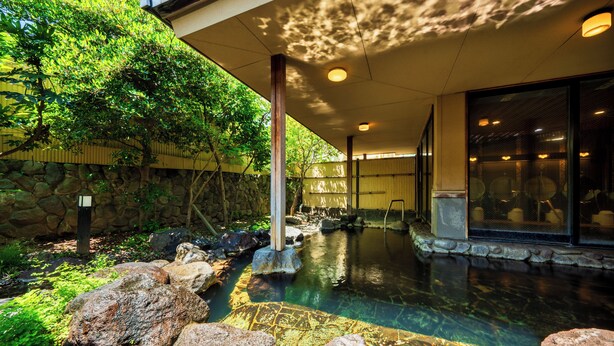A spa area with a hot spring, stone walls, and a covered seating area. - Hana Beppu (Beppu)