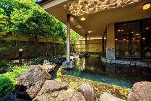 A spa area with a hot spring, stone walls, and a covered seating area. - Hana Beppu (Beppu)