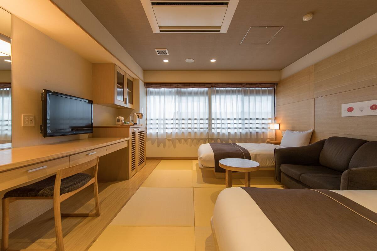 A modern hotel room with a bed, a sofa, a desk, a television, and a window with curtains.