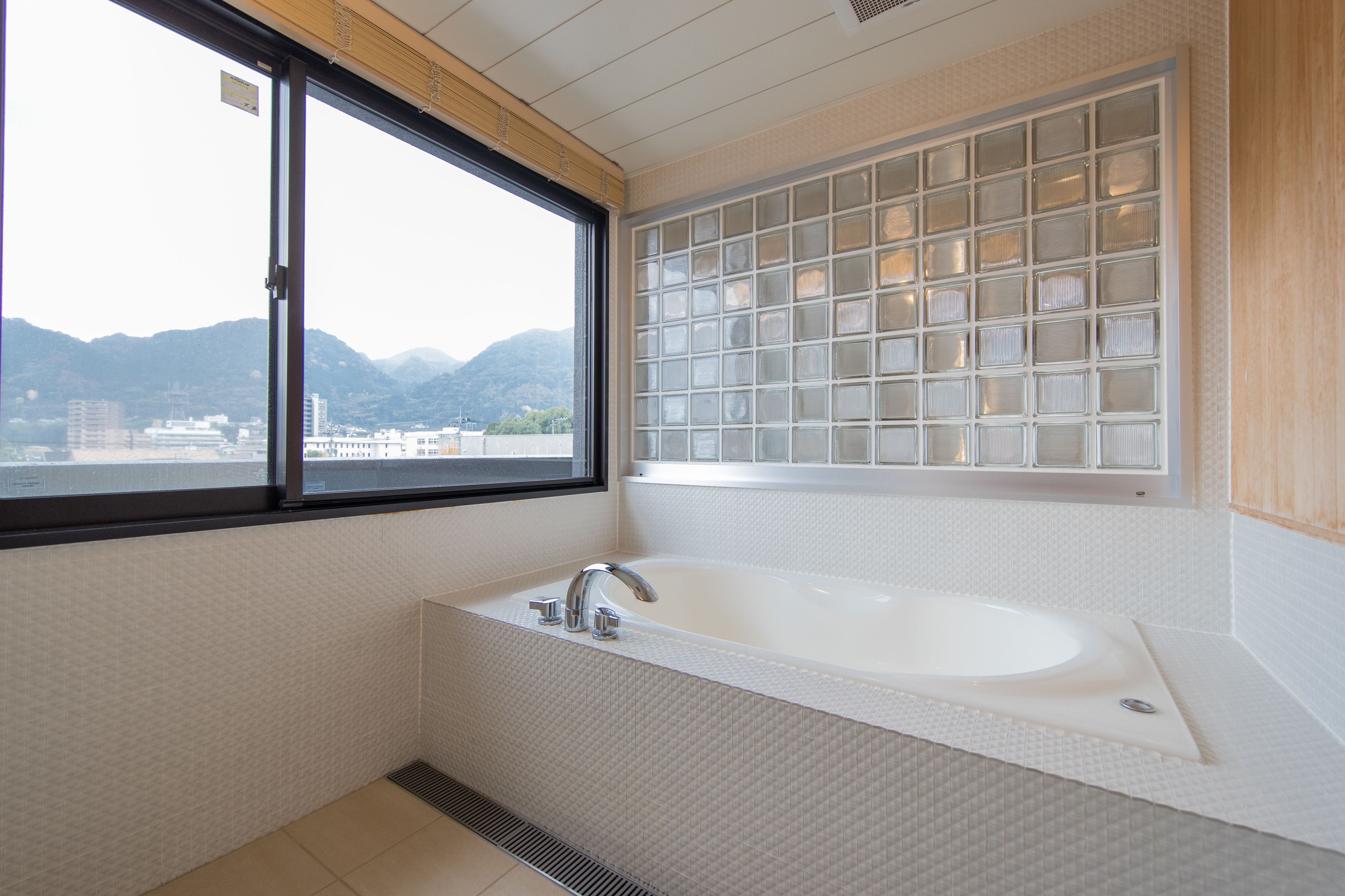Un baño moderno con una bañera grande, una ventana con vistas a las montañas y una pared de bloques de vidrio.