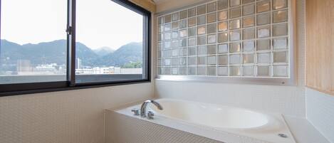 Un baño moderno con una bañera grande, una ventana con vistas a las montañas y una pared de bloques de vidrio.