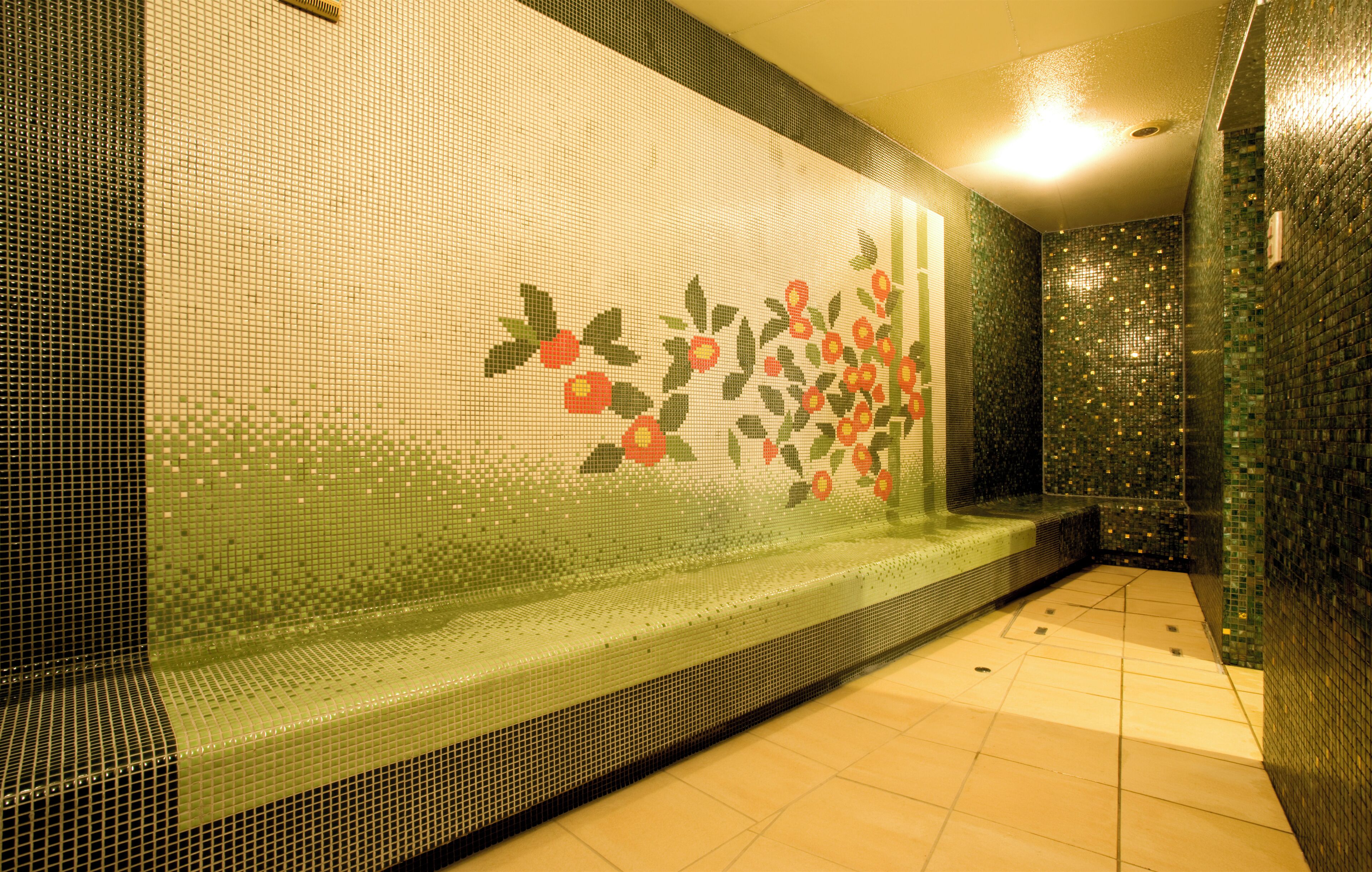 Pared de azulejos con un mosaico de elementos rojos y verdes, un banco y un suelo de azulejos.