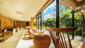 A modern interior with large windows, wicker furniture, and a view of greenery outside. - Hana Beppu (Beppu)