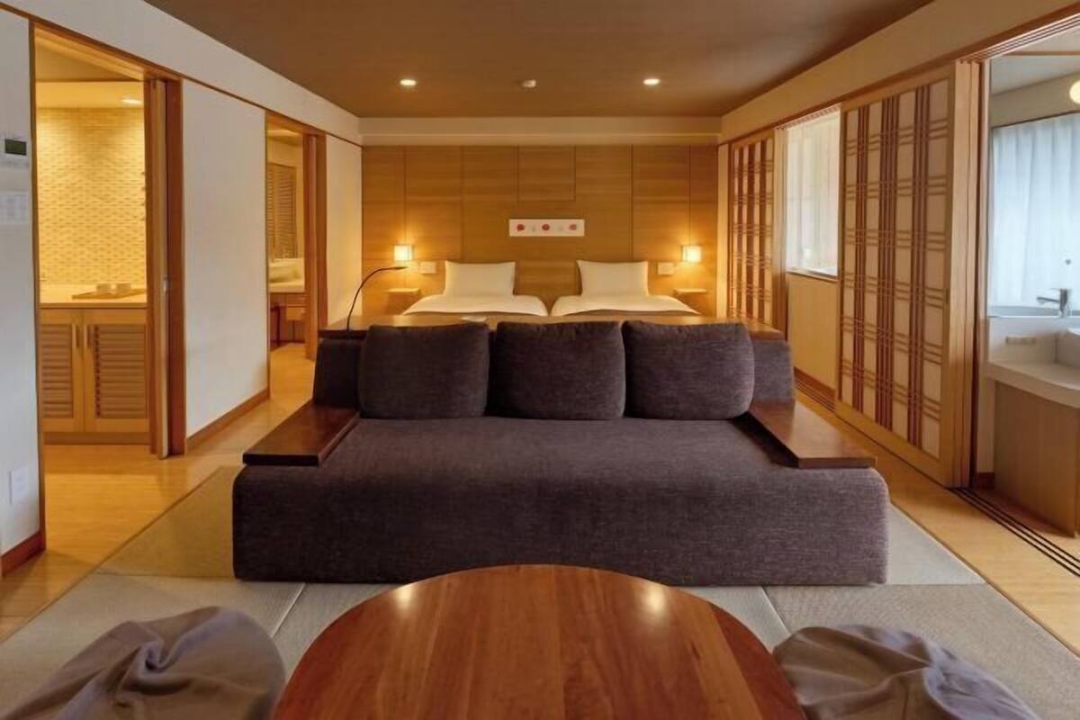 A modern hotel room with a sofa bed, a wooden coffee table, and traditional sliding doors.