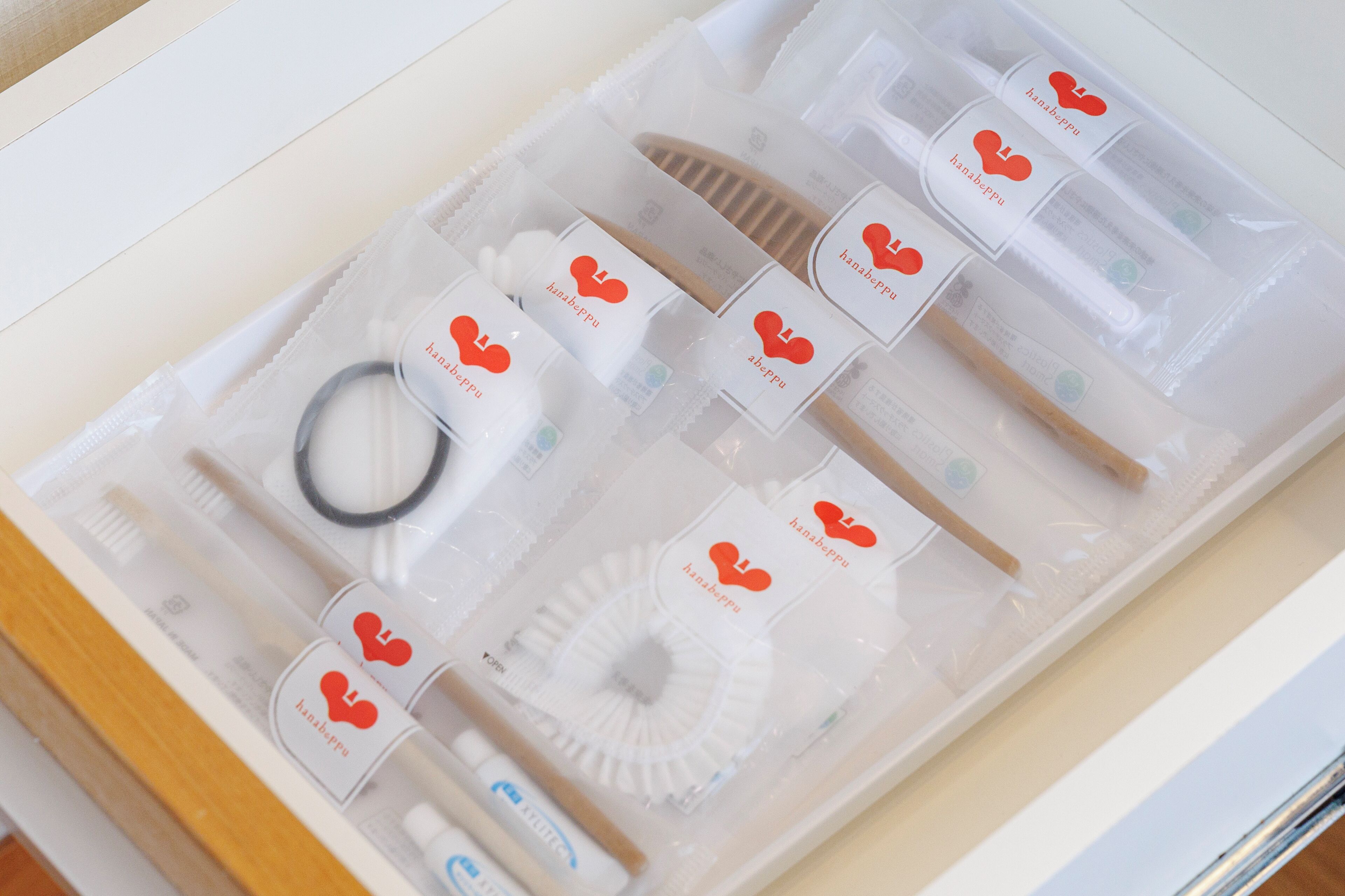Un cajón ordenado con varios artículos de cuidado personal, como cepillos de dientes, pasta dental e hilo dental, todos envueltos en plástico transparente con etiquetas.