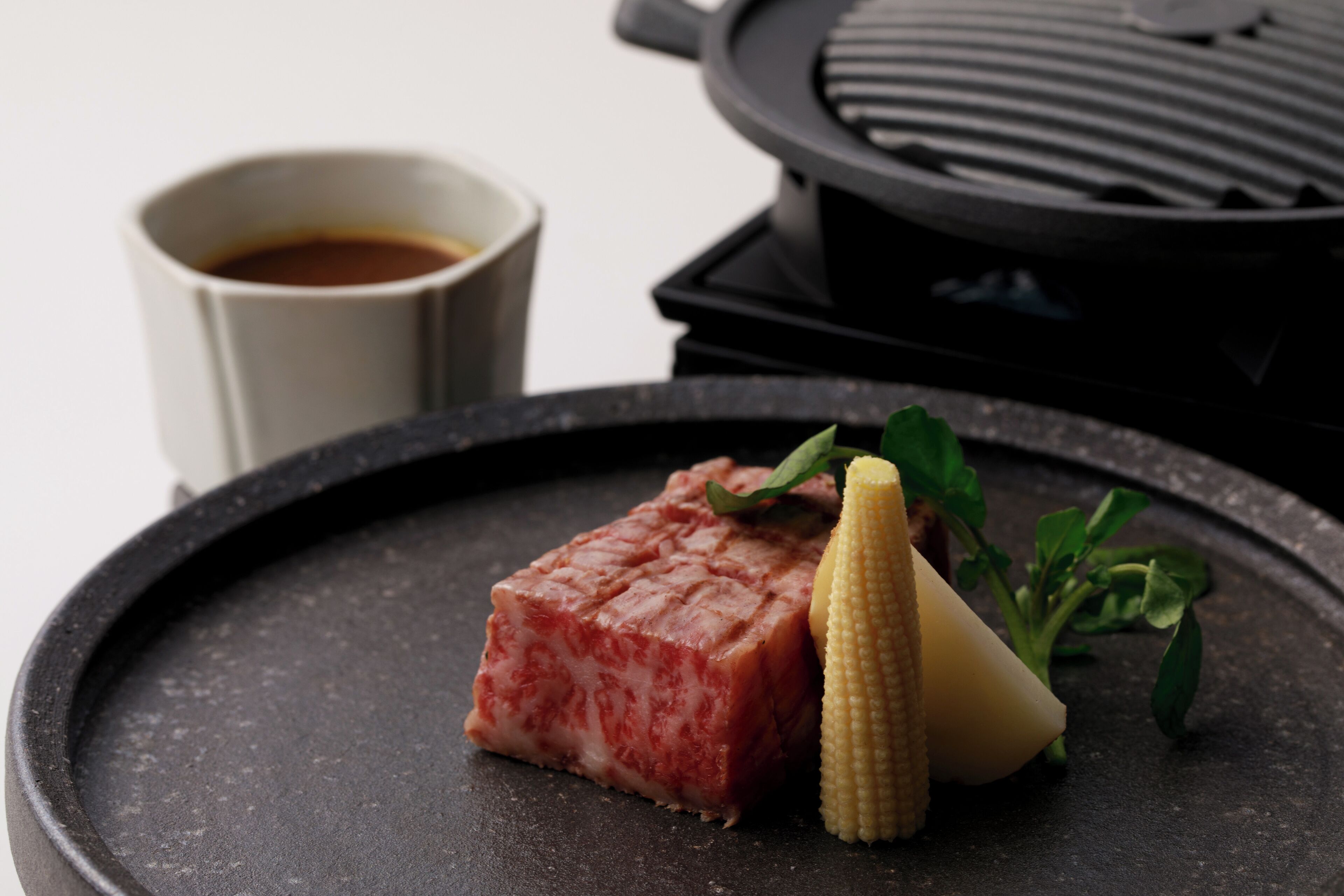 A grilled steak, corn, and a cup of coffee on a black plate.