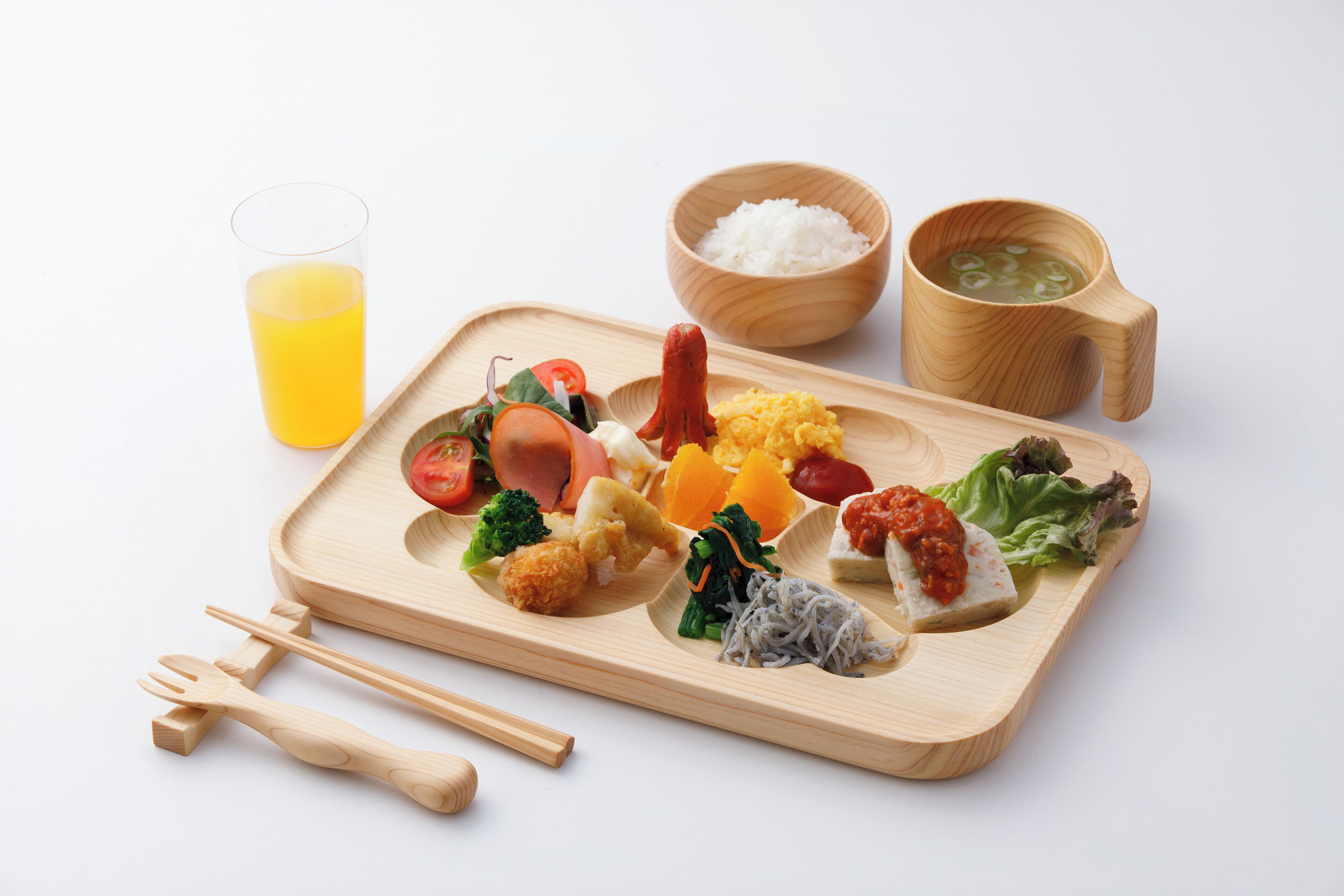 A wooden tray with various food items, a glass of orange juice, and wooden bowls.