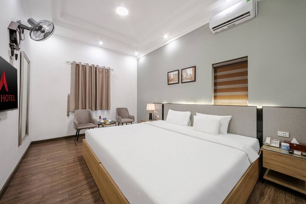 Ein Hotelzimmer mit einem großen Bett, zwei Sesseln, einem Schreibtisch mit Lampe und einer Klimaanlage.