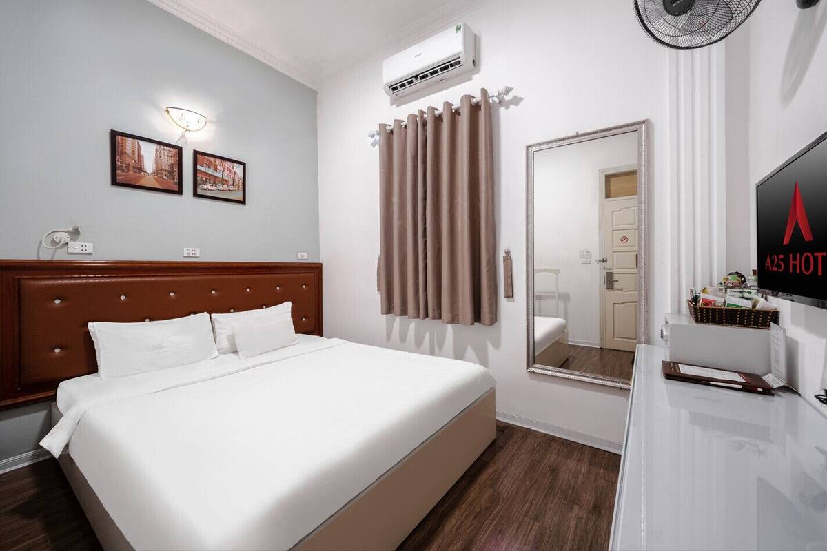 Ein Hotelzimmer mit einem großen Bett, einem Nachttisch, einem Spiegel, einer Klimaanlage und einem an der Wand befestigten Fernseher.