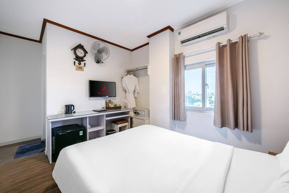 Ein Hotelzimmer mit einem Bett, einem Schreibtisch mit Fernseher, einer Uhr, einem Ventilator und einem Fenster mit Vorhängen.