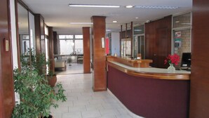 A reception area with a curved reception desk, a potted plant, and a window with a view of the outside. - Hotel Royal (Córdoba)