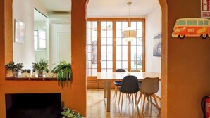 A dining area with a wooden table and chairs, a TV on a stand, and potted plants. - Charming Patio by Hello Homes Sitges (Sitges)