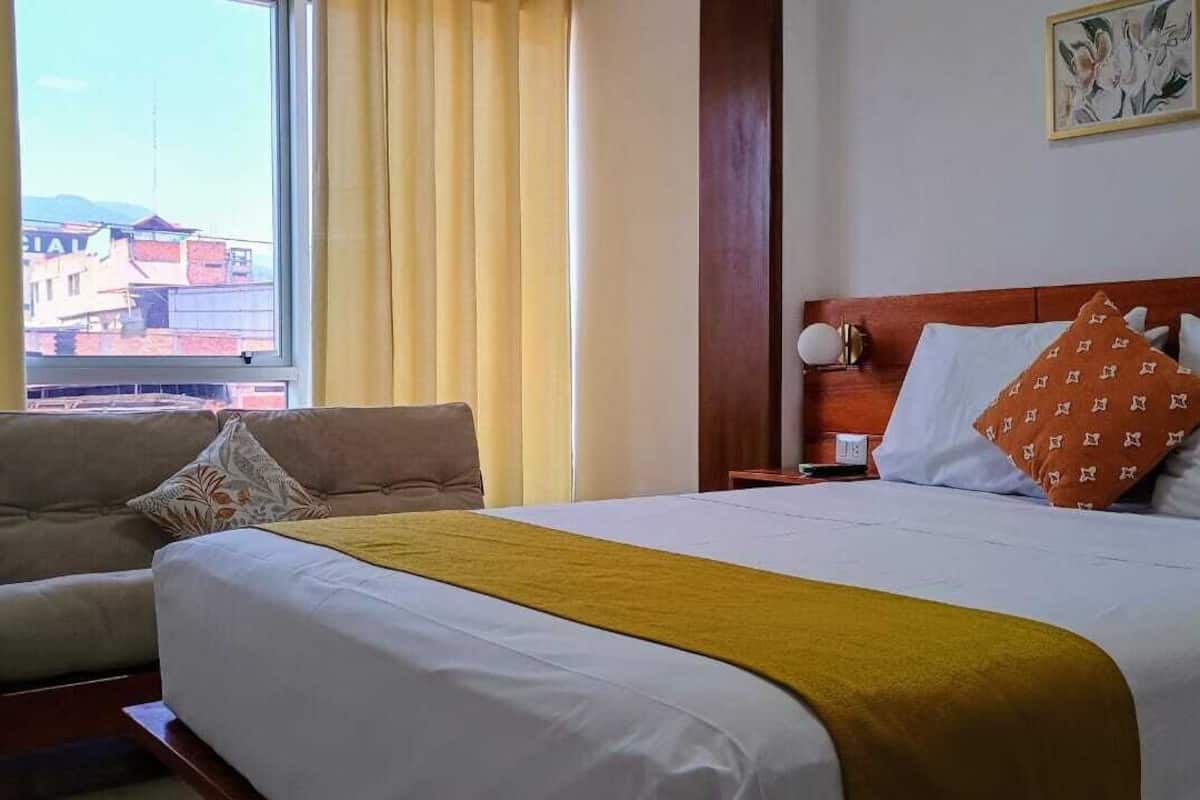 A hotel room with a bed, a sofa, a nightstand, and a window with curtains.