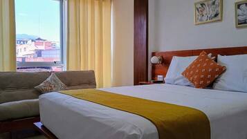 Una habitación de hotel con cama, sofá, mesita de noche y ventana con cortinas.