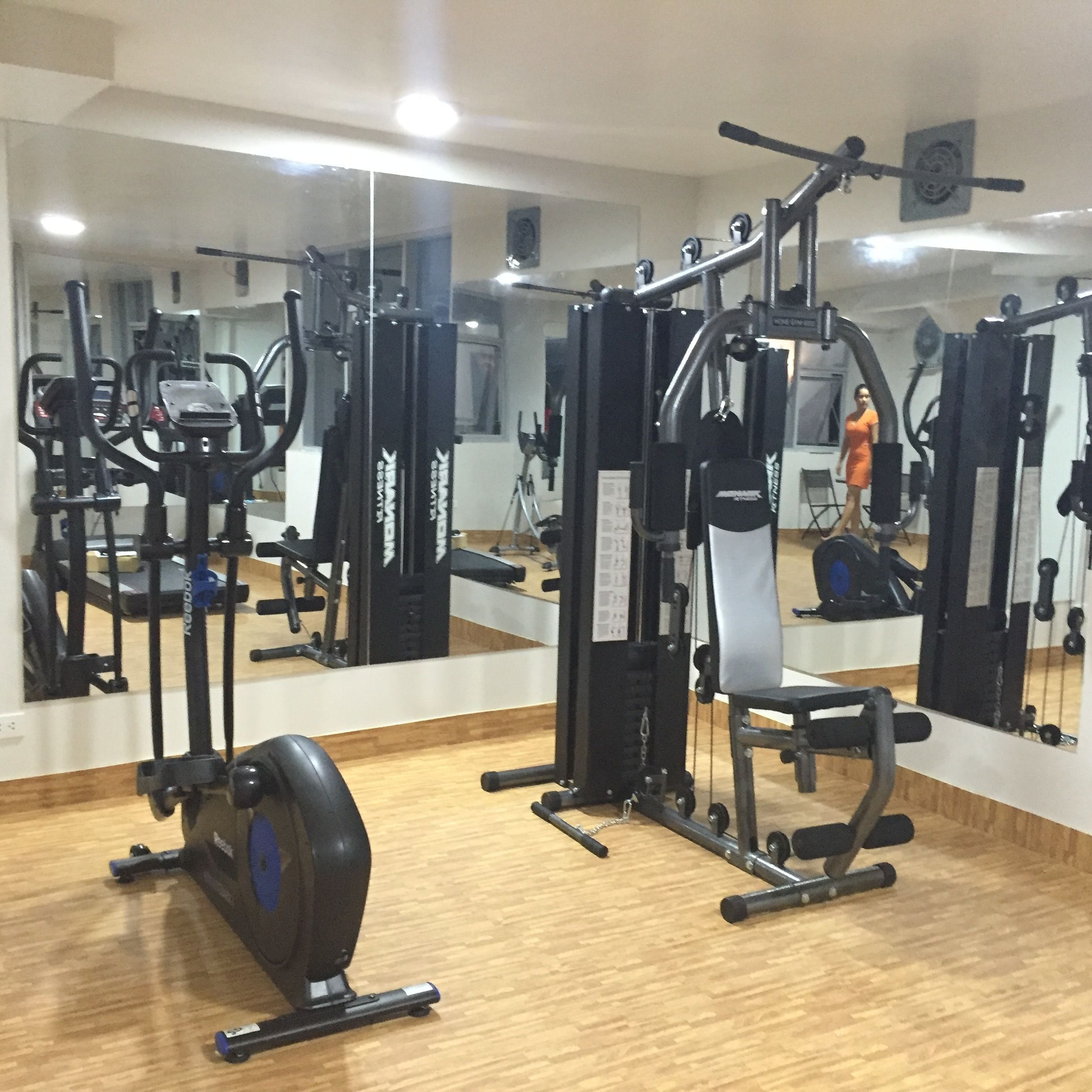 A gym with various exercise machines, a mirrored wall, and a wooden floor.