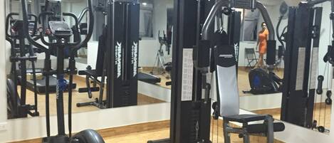 A gym with various exercise machines, a mirrored wall, and a wooden floor.