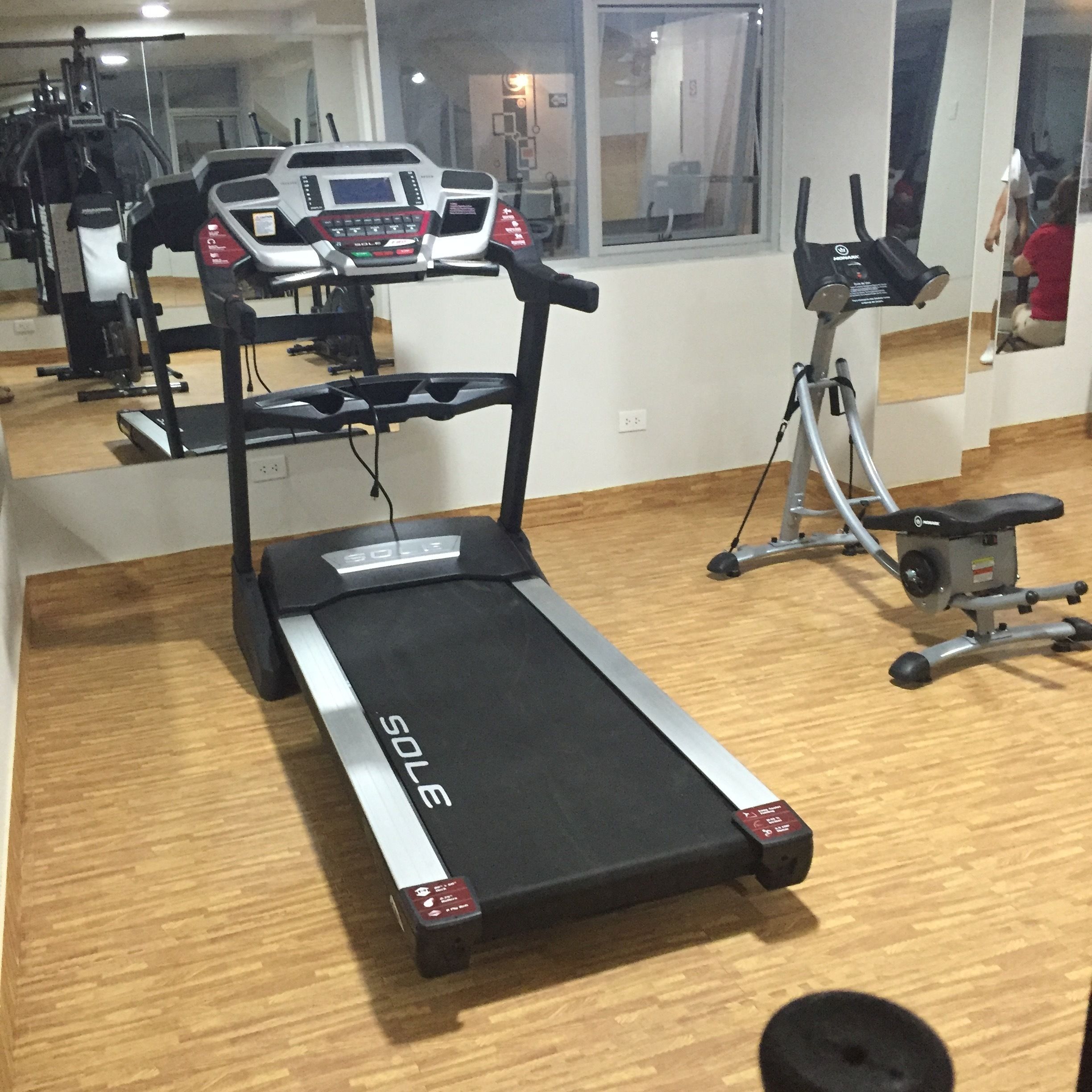 Un gimnasio con cinta de correr, bicicleta estática y banco para pesas.