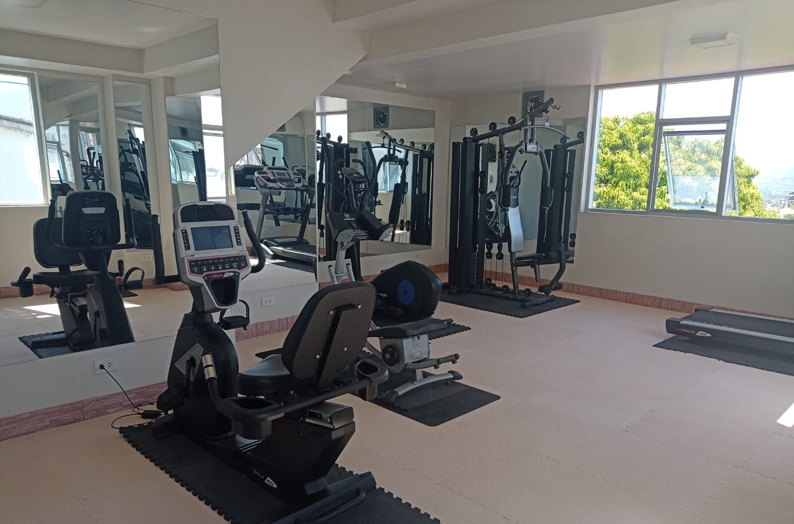 Une salle de sport équipée de machines de cardio, de matériel d’entraînement en force et de miroirs aux murs.