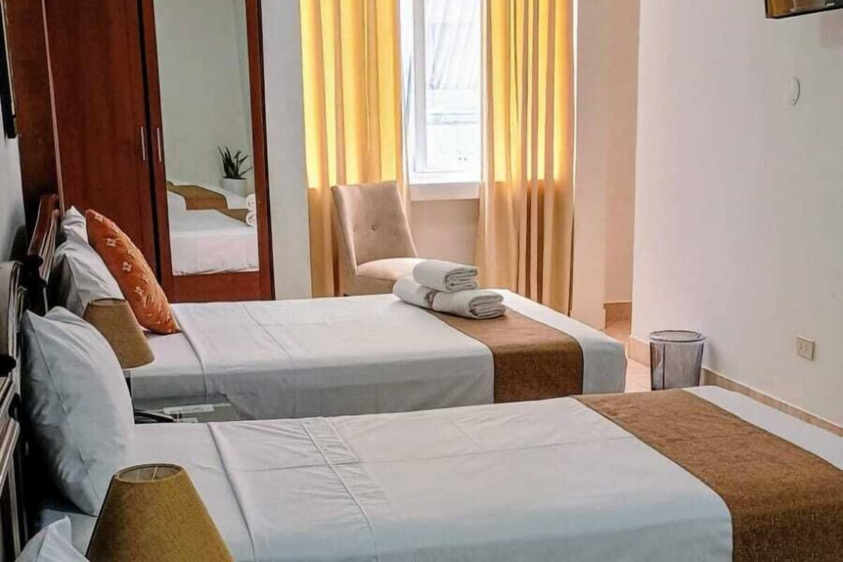 A hotel room with two beds, a mirror, a TV, and a window with curtains.