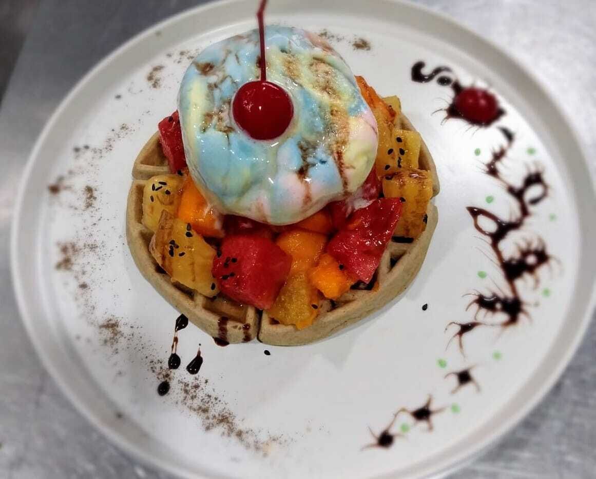 A dessert with a waffle, fruit, and a cherry on a white plate.