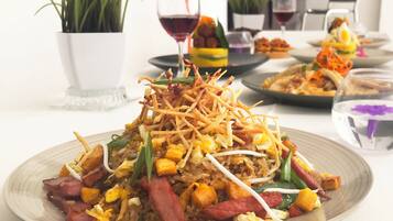 A dining table with multiple plates of food, including a dish with rice, vegetables, and meat. There are potted plants and a wine glass on the table.